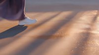 Golden sandy beach with diagonal shadows cast by a person walking along the shoreline at sunset, creating a serene coastal atmosphere.