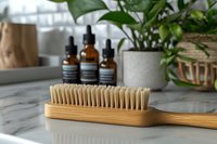 Natural bamboo brush with bristles on marble counter, essential oil bottles and green plants in background creating eco-friendly bathroom atmosphere.