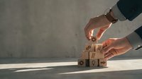 Business professional hands protecting wooden blocks with fragile shipping symbols representing logistics risk management and cargo insurance concepts.