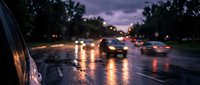 Rainy evening traffic with wet asphalt reflecting car headlights and street illumination during twilight hours creating atmospheric urban driving conditions.