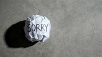 Crumpled paper ball with the word Sorry written on it lying on a concrete floor, symbolizing regret, apology, and failed communication.