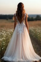 Young bride in luxurious lace wedding dress with open back poses in wildflower meadow during golden hour sunset, long brown hair flowing naturally down her back.