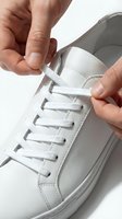 Caucasian male hands tying white laces on a clean leather sneaker against a light background, capturing a fresh, minimal style moment.