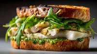 Gourmet sandwich with grilled chicken, fresh arugula and pesto on artisan bread. Delicious lunch meal for restaurant menu or food blog content.