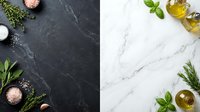 Overhead view of dark slate and white marble surfaces with fresh herbs, olive oil, and sea salt arranged for culinary styling and food preparation concepts.
