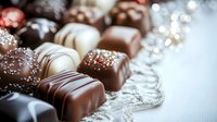Assorted luxury chocolate pralines with dark, milk and white chocolate decorations on white wooden background with silver festive garland and bokeh lights.