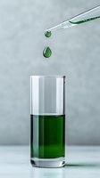 Green liquid drops falling from pipette into tall glass cylinder on gray background, scientific laboratory research concept for chemistry experiments.