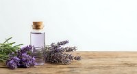 Lavender essential oil bottle with cork stopper and fresh purple lavender flowers on rustic wooden table for aromatherapy and natural wellness.