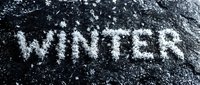 Word WINTER written with snow on dark stone surface, cold season concept with snowflakes, frosty texture background for seasonal design.