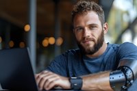 Caucasian male podcaster or content creator with beard wearing blue shirt, working at laptop with microphone in modern studio setting for broadcasting or recording.