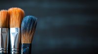 Professional makeup brushes with soft bristles in orange and black colors against dark background, closeup view with copy space for beauty and cosmetics industry.