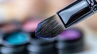 Professional makeup brush with soft bristles over colorful eyeshadow palette for beauty and cosmetics application in studio lighting.