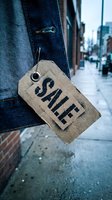 Rustic cardboard sale tag hanging on denim jeans on a rainy urban street, evoking fashion retail discount and seasonal shopping concepts.