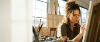 Young woman artist painting on canvas in bright art studio with easel and brushes creating artwork in creative workspace.