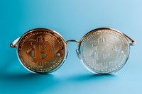Round eyeglasses with gold and silver bitcoin coins as lenses on turquoise background, creative cryptocurrency concept for financial vision and investment perspective.