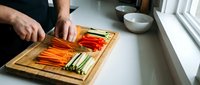 Male chef preparing colorful fresh vegetables on wooden cutting board in modern kitchen for healthy cooking and meal preparation.