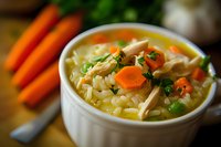 Homemade chicken noodle soup with tender carrots, orzo pasta and fresh herbs in white ceramic bowl. Comforting traditional recipe for cold weather meals.