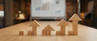 Wooden blocks arranged in ascending growth pattern on office desk with business charts in background representing financial progress and development.