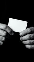 Elderly hands holding blank white business card against black background in monochrome style for corporate identity and branding design projects.