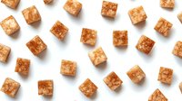 Brown sugar cubes scattered on white background creating geometric pattern, sweet crystallized ingredients for cooking and beverages, isolated objects.