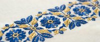 Traditional blue and gold floral embroidery on white fabric featuring decorative flowers and leaves in ethnic folk art style for textile design projects.