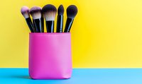 Professional makeup brushes in pink holder against vibrant yellow and blue background. Minimal beauty concept with copy space for text or design.