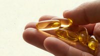 Close-up of hand holding golden gel capsules, supplements or vitamins for health and wellness products, nutrition and dietary supplements.