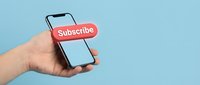 Hand holding smartphone with red subscribe button on light blue background, social media and digital marketing concept.