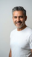 Handsome mature Hispanic man with gray hair and beard smiling warmly in white t-shirt against neutral background for lifestyle and wellness content.