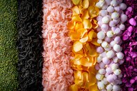Colorful rows of artificial flower petals and decorative elements in vibrant green, black, pink, yellow, white, and purple creating striking pattern for craft projects.