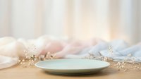 Mint green empty plate on wooden table with dried flowers and soft pastel fabrics, suitable for styling food photography, table settings, and home decor projects.