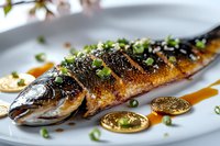 Grilled whole mackerel garnished with black sesame seeds and green onions on white plate with soy sauce reduction, styled for upscale Asian restaurant presentation.