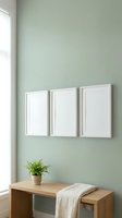 Three blank white frames on a sage green wall above a wooden console table with a fern plant, mockup for art print or poster display.