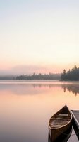 Wooden rowboat moored at dock on calm lake at sunrise with misty forest treeline reflected in still water, peaceful morning landscape for travel and nature projects.