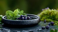 Fresh blueberries in rustic black bowl with mint leaves on moss-covered surface. Organic superfood harvest concept for healthy eating and natural nutrition.