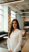Professional brunette businesswoman in white shirt standing in modern office with geometric patterns and natural lighting for corporate presentations.