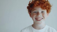 Cheerful redhead boy with freckles smiling broadly, wearing a white t-shirt against a light background, copy space for text.