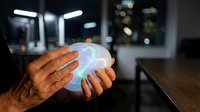 Close-up of hands holding glowing holographic sphere with digital light effects in modern office environment at night for technology and innovation concepts.