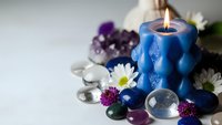 Blue candle burning among healing crystals, gemstones and white flowers creating peaceful spa meditation atmosphere for wellness and relaxation rituals.