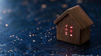 Wooden smart home model with glowing red lights on circuit board background, representing IoT and home automation technology integration.