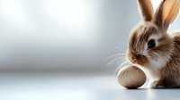 Adorable brown bunny rabbit with long ears sitting next to a speckled egg against soft blurred background, perfect for Easter holiday designs.