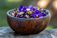 Wooden bowl filled with mixed nuts and purple pansy flowers on rustic stone surface with natural outdoor lighting for healthy eating concepts.