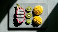 Sliced dragon fruit, kiwi, and mango arranged on a stone board in bright sunlight, showcasing vibrant tropical colors and fresh summer nutrition.