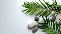 Fresh palm leaves with smooth zen stones arranged on light gray background, creating minimalist spa and wellness composition for relaxation and meditation practices.