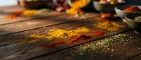 Colorful spices scattered on rustic wooden table with bowls in background creating vibrant culinary scene for cooking and food preparation concepts.