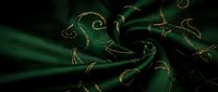 Luxurious emerald green silk fabric with golden embroidered swirls and decorative patterns, flowing textile material for fashion and interior design projects.