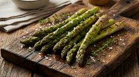 Fresh green asparagus spears with sea salt on rustic wooden cutting board, ready for cooking or meal preparation.