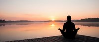 Person in silhouette meditating on wooden dock at sunrise over calm lake, peaceful morning mindfulness and wellness practice for relaxation and mental health.