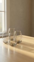 Four empty stemless wine glasses arranged on wooden table near window with warm natural light creating elegant dining atmosphere for entertaining.