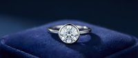 Elegant diamond solitaire engagement ring with brilliant cut stone in white gold setting on luxury blue velvet jewelry box background.